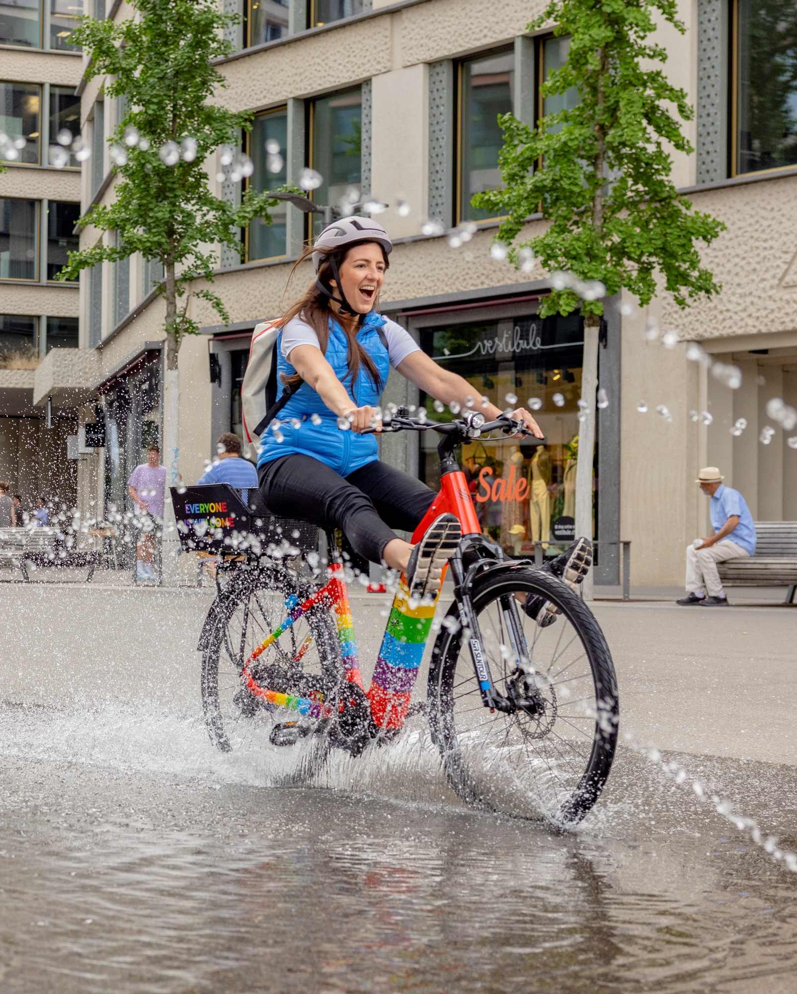 Radfahrerin auf E-Bike, fährt durch Wasserfontäne